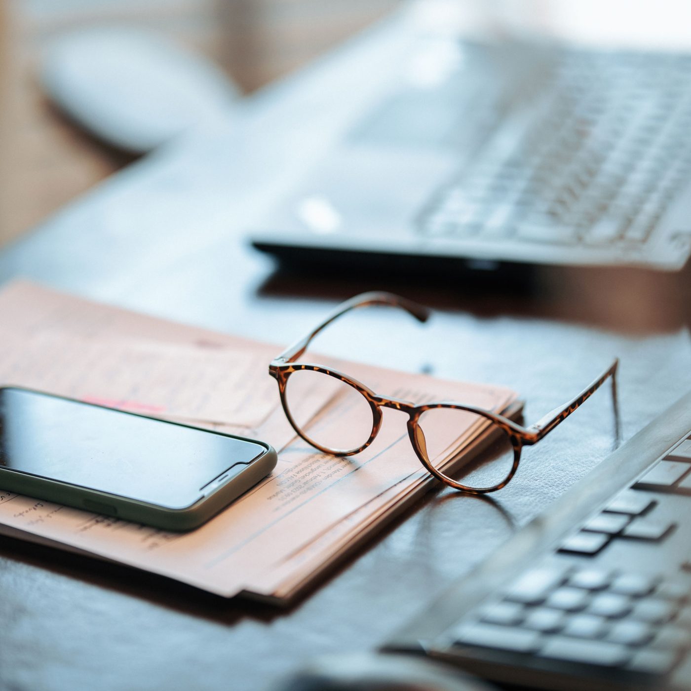 Brille und Smartphone liegen auf Schreibtisch